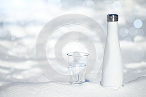 . A glass of pure blue water and a metal bottle on a snowy background. The concept of clean, healthy water, zero waste, no plastic