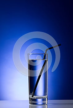 Glass with pure water with a black straw on a blue