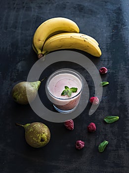 Glass of raspberry and pear smoothie with fresh mint leaves on black