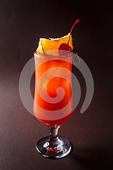Glass of red alcohol cocktail with cherry, slice of orange and s