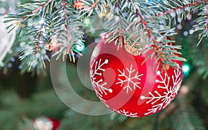 Glass red ball on blurred christmas tree background with holiday lights