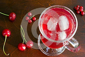 A glass of red cherry juice with ice cubes and cherries and red currants on a wooden background closeup