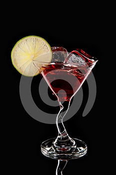 Glass of red cocktail with ice cubes and lime