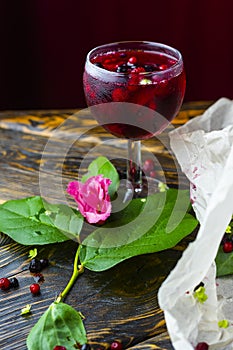 A glass with a red drink with berries, ice and a pink flower on