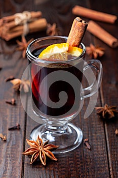 Glass of red glogg or mulled wine with orange slices and cinnamon stick on dark wooden background, vertical