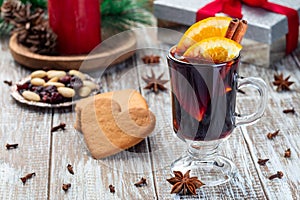 Glass of red glogg or mulled wine with orange slices and cinnamon stick, gingerbread cookies and gift box on background,