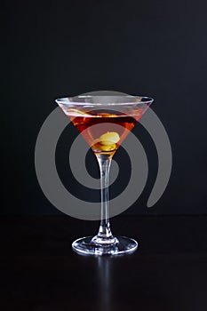 A glass of red martini with olives on a dark background