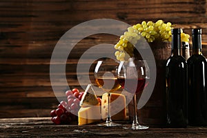 Glass of red and white wine, cheeses and grapes on brown wooden background