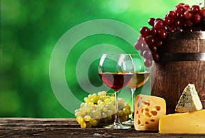 Glass of red and white wine, cheeses and grapes on the brown wooden background