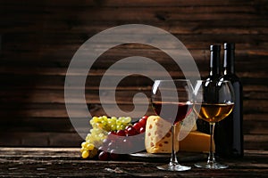 Glass of red and white wine, cheeses and grapes on the brown wooden background