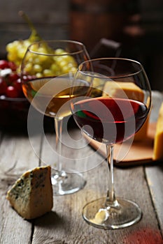 Glass of red and white wine, cheeses and grapes on a grey wooden background