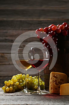 Glass of red and white wine, cheeses and grapes on the grey wooden background