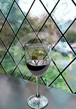 Glass of red wine against stained glass window with leaded crisscross pattern.