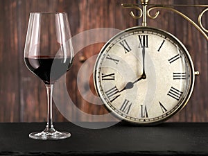 Glass of red wine with antique clock on wooden background, concept image for dinner time