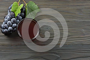Glass of red wine with blue grapes and green leaf on dark wooden table. Top view with copy space