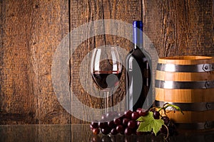 Glass of red wine with bottle barrel grapes on glass