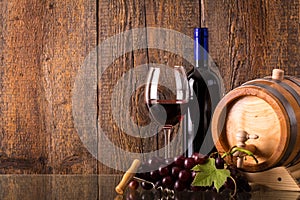 Glass of red wine with bottle barrel grapes and wooden background