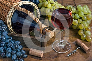 Glass with red wine,  bottle, bunch of grapes,  corkscrew on  wooden table