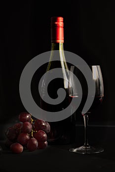 Glass of red wine with a bottle, cluster of grapes