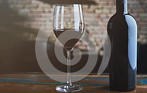 Glass of red wine and wine bottle on colorful wooden table at home, brick wall in the background