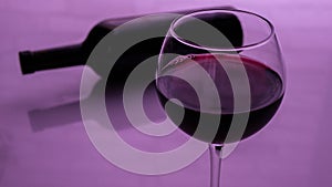 A glass of red wine with a bottle on a pink background.
