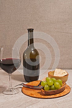 Glass of red wine, bottle, and rare wood plate with corkscrew and  of green grapes
