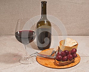 Glass of red wine, bottle,  and rare wood plate with corkscrew and  of red grapes