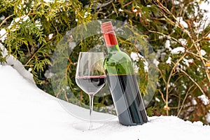 A glass of red wine and  bottle of wine in snow