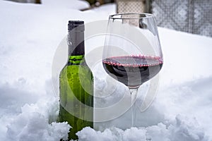 A glass of red wine and  bottle of wine in snow