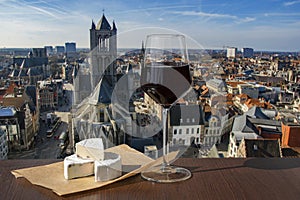 Glass of red wine with brie cheese against view of big cathedral in Ghent, Belgium