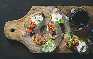 Glass of red wine, brushetta with vegetables, cream-cheese, arugula