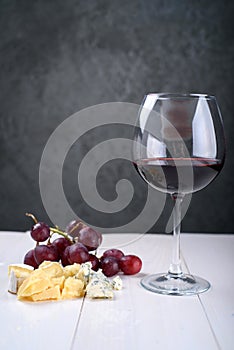 A glass of red wine, a bunch of grapes and cheese