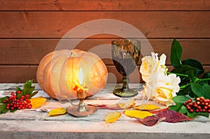 Glass of red wine, burning candle, white roses, pumpkin, autumn leaves and viburnum berries. Selective focus