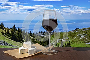 Glass of red wine with cheese against mountains background. View of blue sea and green valley in the mountains