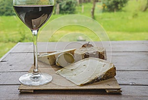 Glass of red wine and cheese on the cutting board on the old wooden table