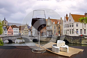 Glass of red wine with cheese snacks against stone bridge in Bruges, Belgium. Traditional bridge over canal in Brugge