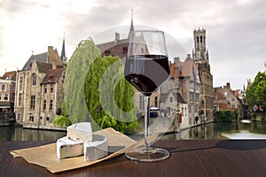 Glass of red wine with cheese snacks against view of Bruges old town and Belfry tower in Bruges, Belgium