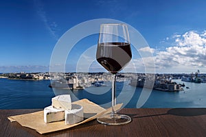 Glass of red wine with cheese with view of city wall and harbor in Valletta, Malta