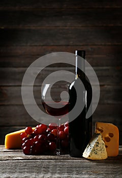 Glass of red wine, cheeses and grapes on the grey wooden background