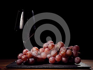 Glass of red wine and cluster of red grapes. Dark background.