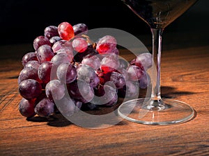 Glass of red wine and cluster of red grapes on a wooden table, dark background. Selective focus