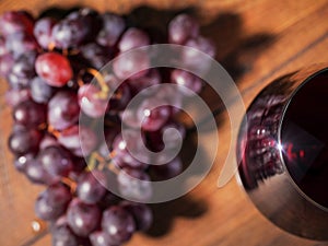 Glass of red wine and cluster of red grapes on a wooden table, top view, selective focus