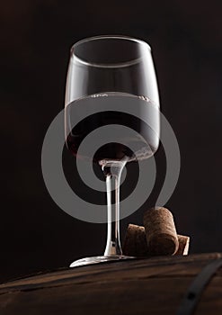 Glass of red wine with corks on top of wooden barrel on black