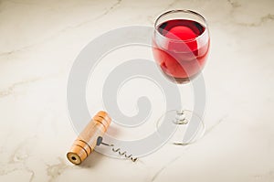 Glass of red wine and corkscrew on white marble background/Glass of red wine and wooden corkscrew on white marble background.