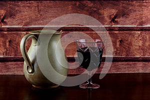 Glass of Red Wine and Earthenware Wine Jug on a Varnished Wooden Shelf