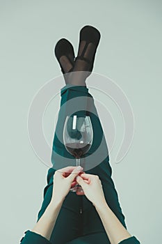 Glass with red wine in female hands against the background of female legs on a gray background
