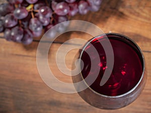 Glass of red wine in focus, cluster of fresh red grapes on a wooden table out of focus, top view