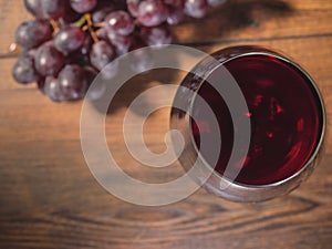 Glass of red wine in focus, cluster of fresh red grapes on a wooden table out of focus, top view