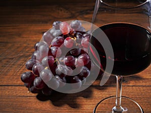 Glass of red wine in focus, cluster of fresh red grapes on a wooden table out of focus, top view