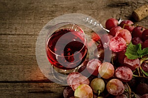 Glass of red wine and Fresh ripe pink grape on a vintage plate, on an old wooden background. Composition with fruits and drink